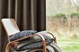 Sessel mit Kissen und Plaid vor Fensterfront mit schwerem Veloursvorhang