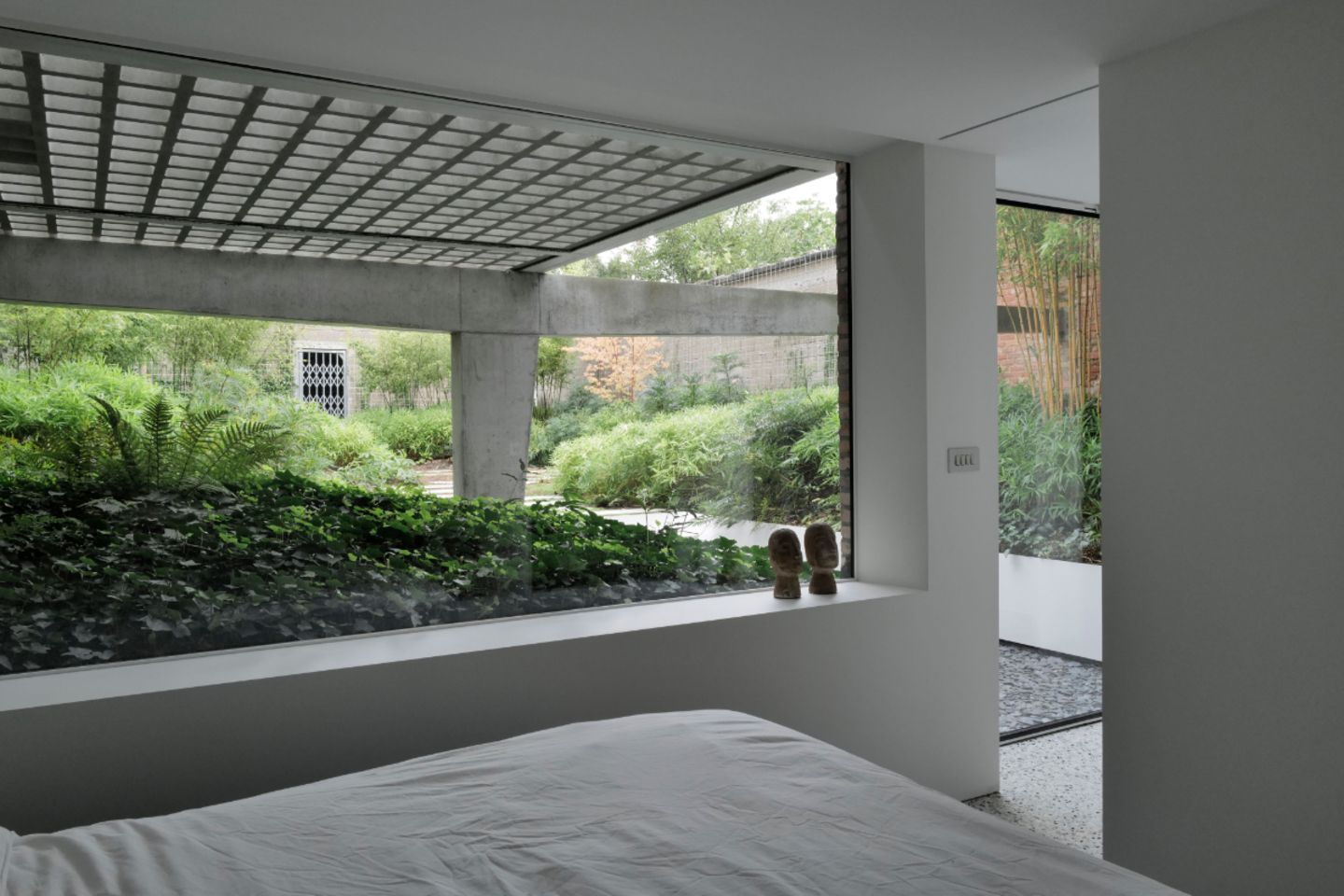 Souterrain-Schlafzimmer mit Blick auf Wintergarten mit viel Grün und Betonkonstruktion mit Terrasse