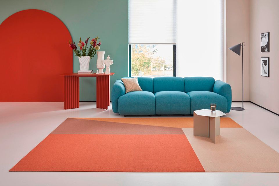 Teppich in Orangetönen vor einem türkisfarbenen Sofa mit einem roten Beistelltisch und weißen Vasen links.