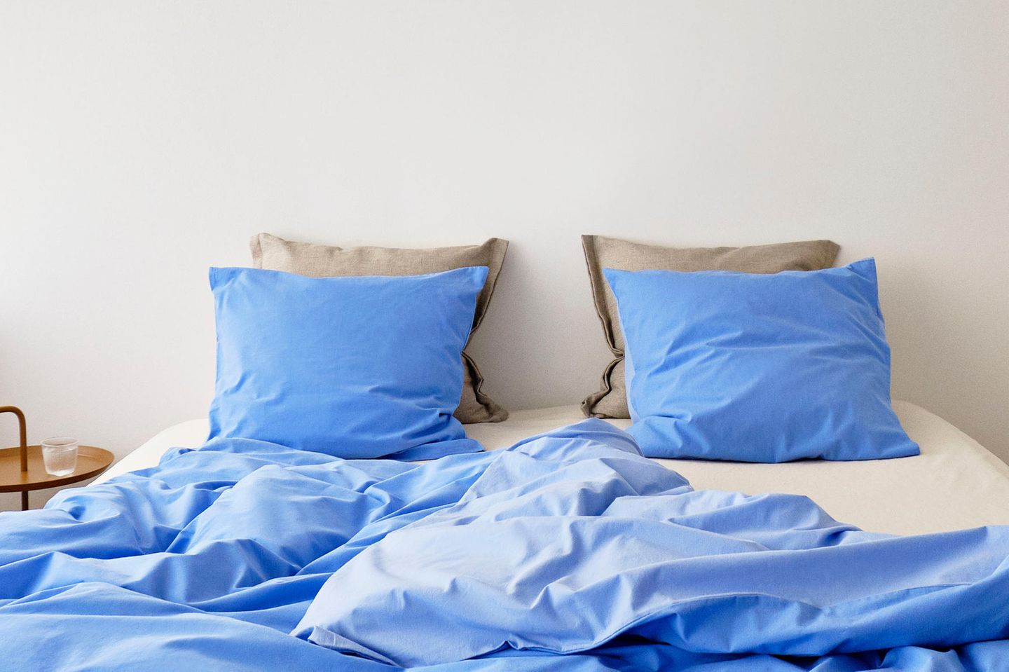 Bettwäsche in Blau in einem ungemachten Bett vor einem weißen Hintergrund