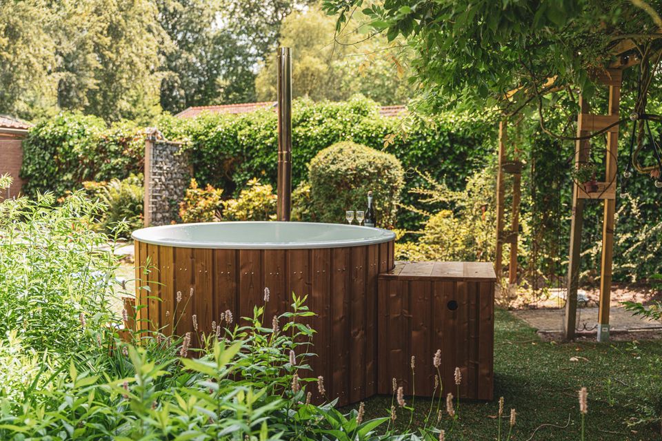 Holz-Pool mit Ofen steht auf einer Terrasse vor Bäumen