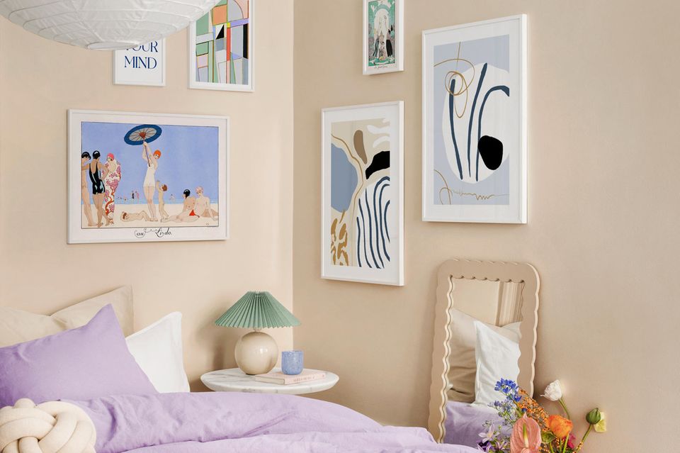 Bett mit bunter Bettwäsche, darüber beige Wand mit bunten Bildern