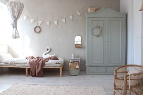 Kinderzimmer mit beiger Wand und salbeigrünem Bauernschrank, dazu Deko und ein Stoff-Schwan, ein Teppich und ein Sessel