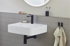 Weißes Waschbecken mit schwarzer Armatur, darüber ein runder Spiegel