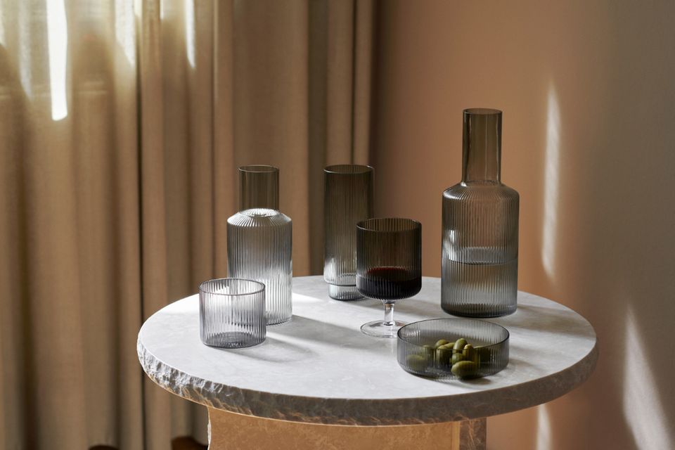 Geriffelte Gläser mit Karaffe und Schälchen mit Oliven auf rundem kleinen Tisch