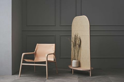Stuhl und Raumtrenner aus Rattan stehen vor einer dunkelgrauen, vertäfelten Wand