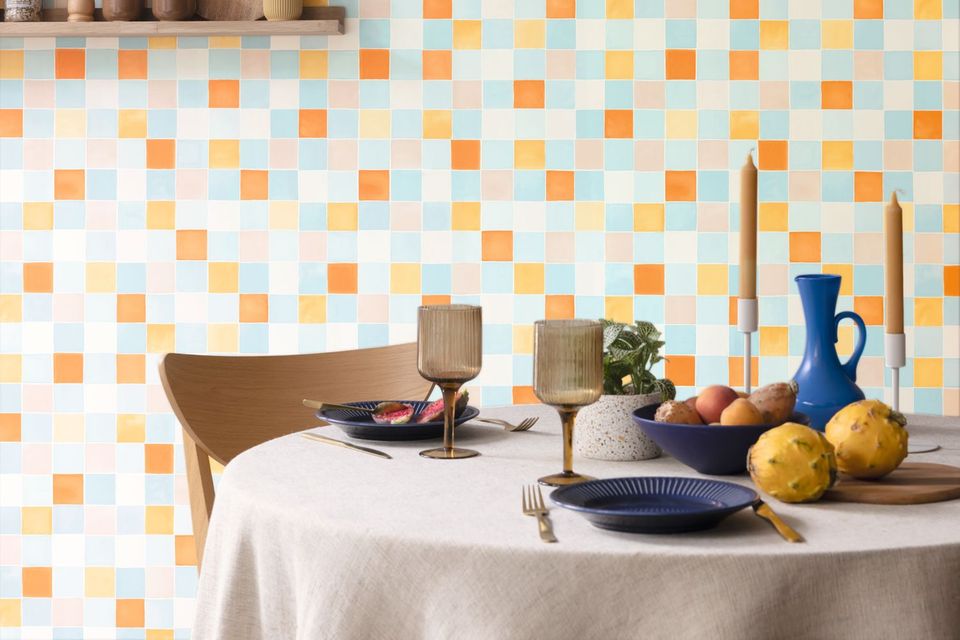 Gedeckter runder Esstisch in gedeckten Farben mit bunter Mosaiktapete im Hintergrund