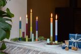 Runder Kerzenständer mit bunten, brennenden Kerzen, dekoriert mit Tannenzweigen und Tannenzapfen