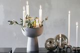 Mit Zweigen dekorierter Kerzenständer mit vier brennenden Kerzen in Form einer Schale in Betonoptik