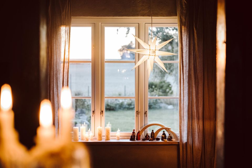 Lichtstern hängt in einem Fenster, darunter Kerzen und weihnachtliche Figuren
