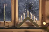 Mintgrüner Lichterbogen mit LED-Kerzen auf einer Fensterbank, daneben eine gedrehte blaue Kerze
