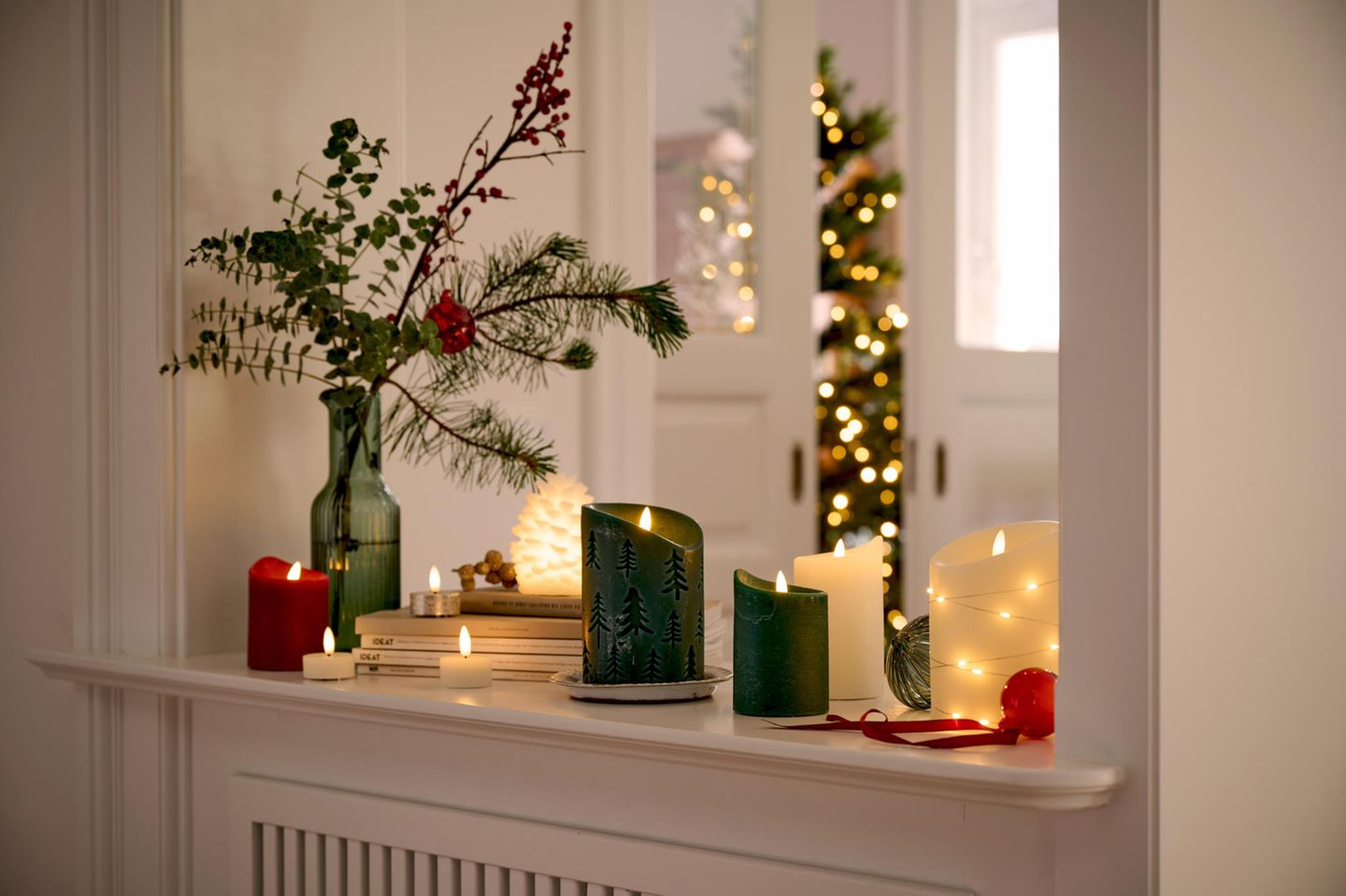 Unterschiedliche Kerzen stehen mit Weihnachtsdeko auf einer Fensterbank