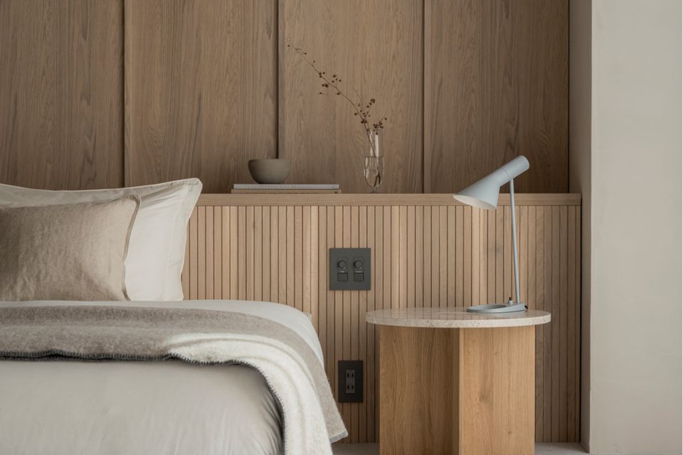 Bett in Schlafzimmer mit holzvertäfelter Rückwand und rundem Beistelltisch aus Holz