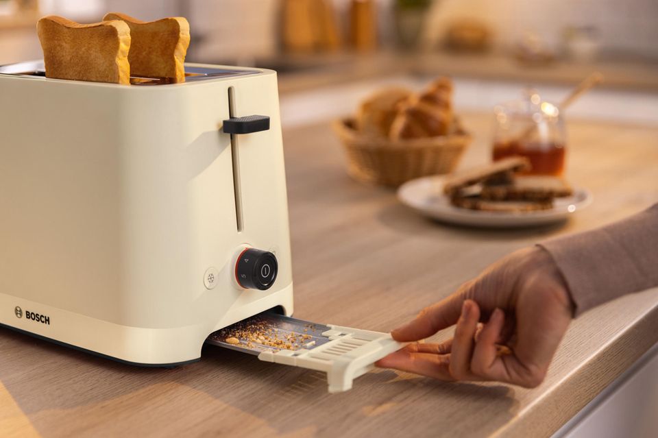 Cremefarbener Toaster steht auf einer Arbeitsplatte, die Krümelschublade wird herausgezogen