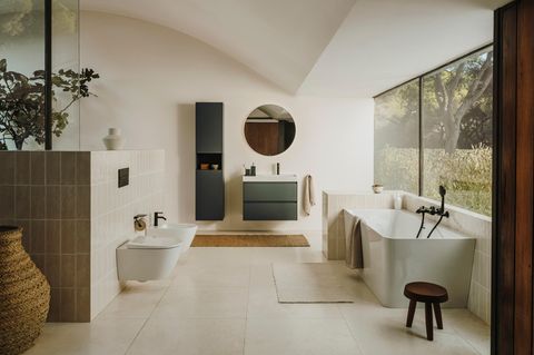 Helles Badezimmer mit Badewanne, Toilette, Bidet und schwarzem Waschtisch sowie großer Fensterfront