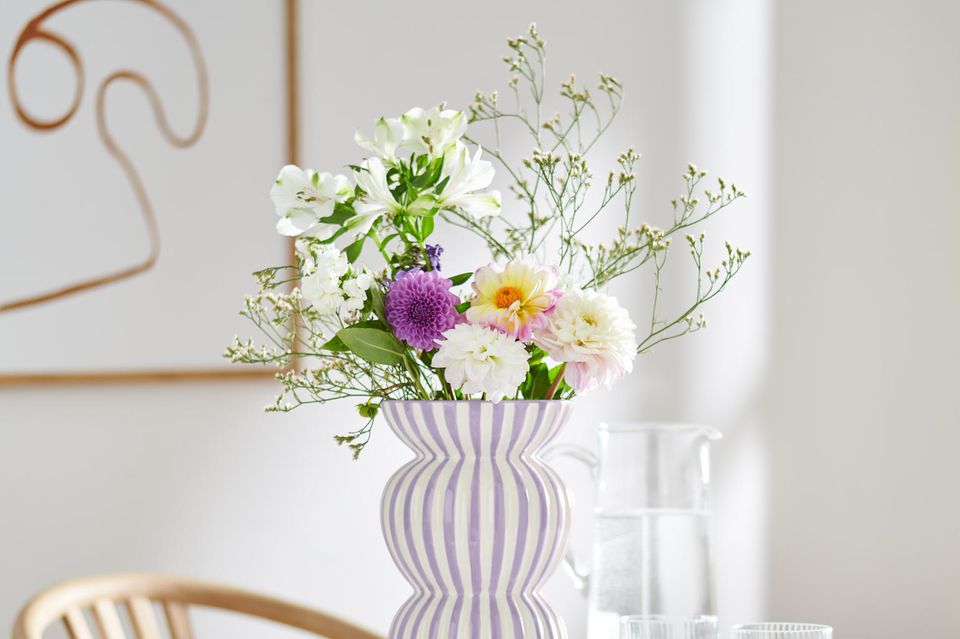 Gestreifte Vase mit Blumen auf einem Tisch mit Tischdecke