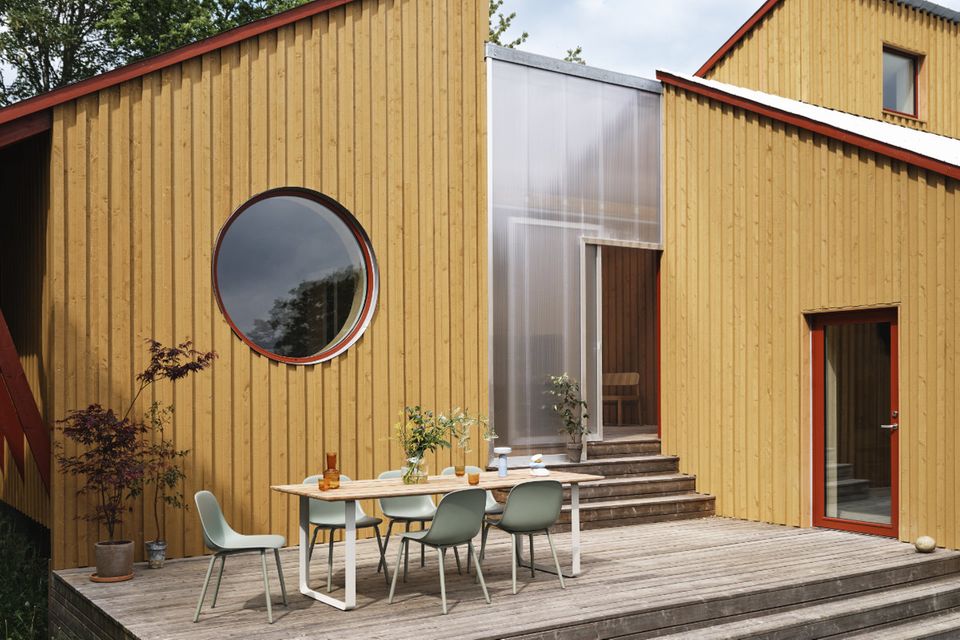 Holzterrasse mit Gartentisch und -stühlen vor Haus mit heller Holzlattenfassade