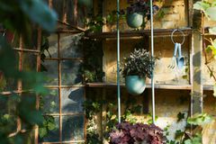 Pflanzenturm in Hellgrün vor der Fassade einer Gartenhütte aus Ziegel mit Regalboards auf denen Pflanzen stehen