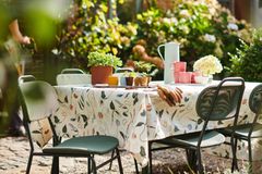 Gartentisch mit einer gemusterten Tischdecke und kleinen Pflanztöpfchen sowie einem Klinkerhaus im Hintergrund