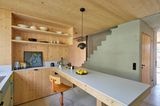 Kücheninsel aus Holz, ein Wandregal aus Holz und dahinter eine Treppe aus Beton