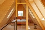 Dachboden mit Holzwänden, Dachfenstern, einem Bett und Glastüren