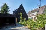 Schwarzes Holzhaus mit Vorgarten, daneben ein helles Haus
