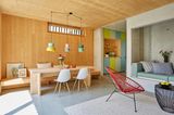 Raum mit beton- und holzwänden, einem einbausofa, Acapulco Stühlen, esstisch aus holz und bunter Küche
