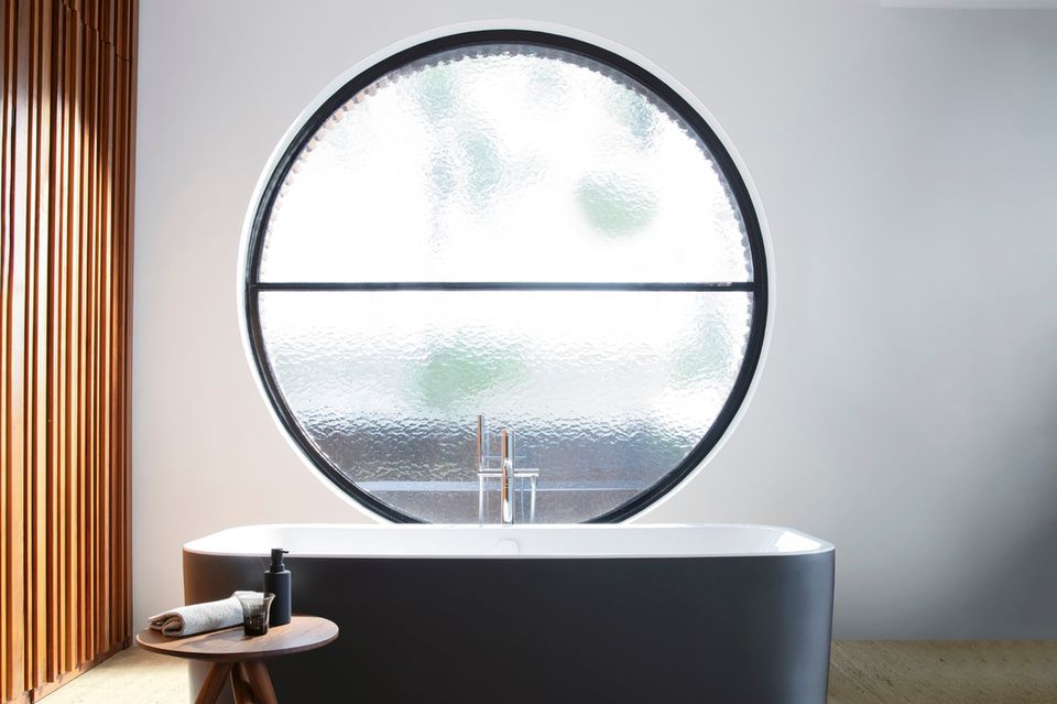 Schwarze Badewanne vor einem runden Fenster mit Strukturglas