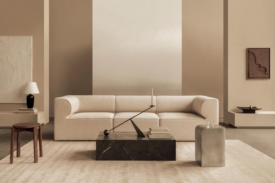 Beige Couch vor beiger Wand, davor schwarzer Tisch aus Marmor mit Deko