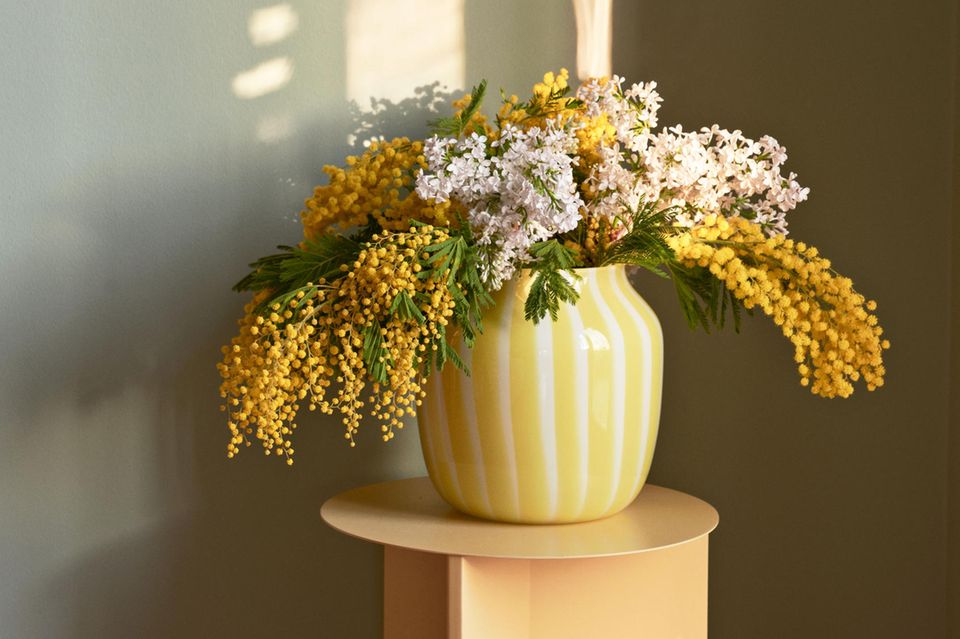 Gelb-Weiß gestreifte Vase auf einem Beistelltisch mit Blumen vor einer Grauen Wand