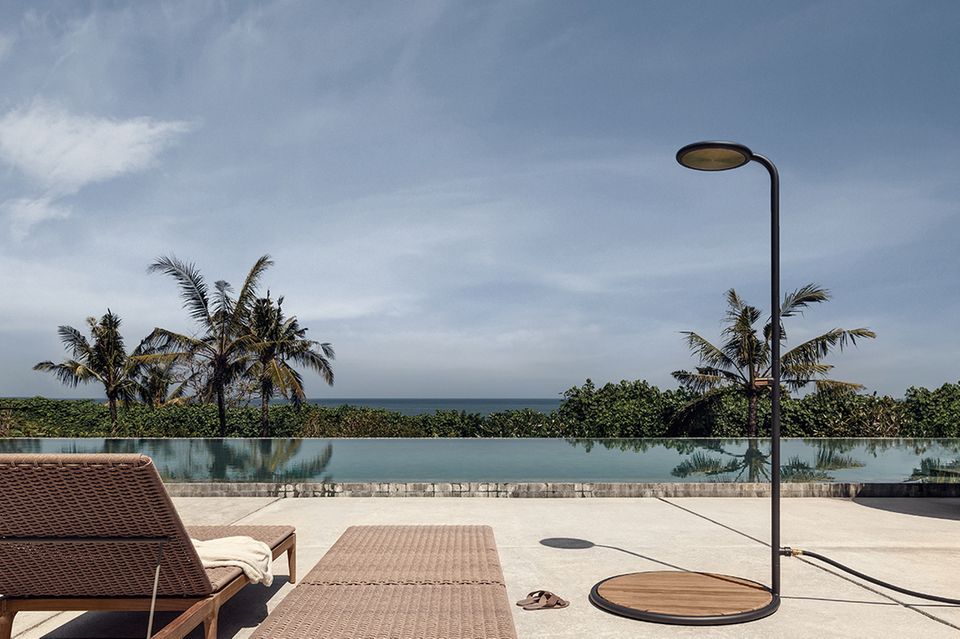 Paradiesischer Blick von oben auf Palmen und Meer, rechts am Rand steht eine hochwertige Gartendusche aus Teak und Aluminium