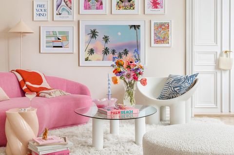 Wohnzimmer mit heller Wand, rosa Couch, bunten Bildern an der Wand und flauschigem weißen Teppich