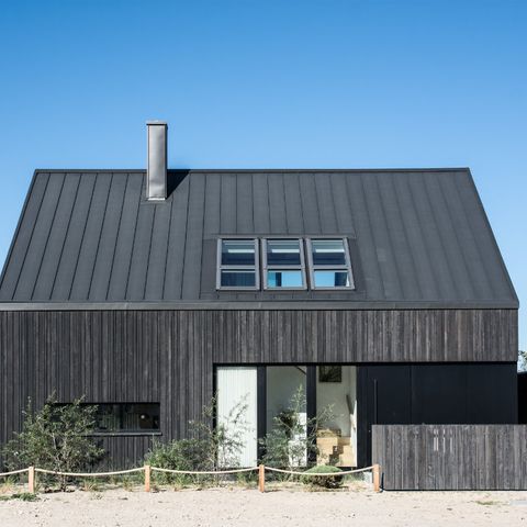Schwarzes Holzhaus vor blauem Himmel auf Dünensand