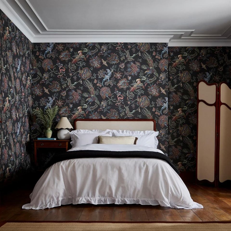 Dunkle florale Tapete hinter einem Bett mit weißer Bettwäsche in einem klassisch eingerichteten Schlafzimmer